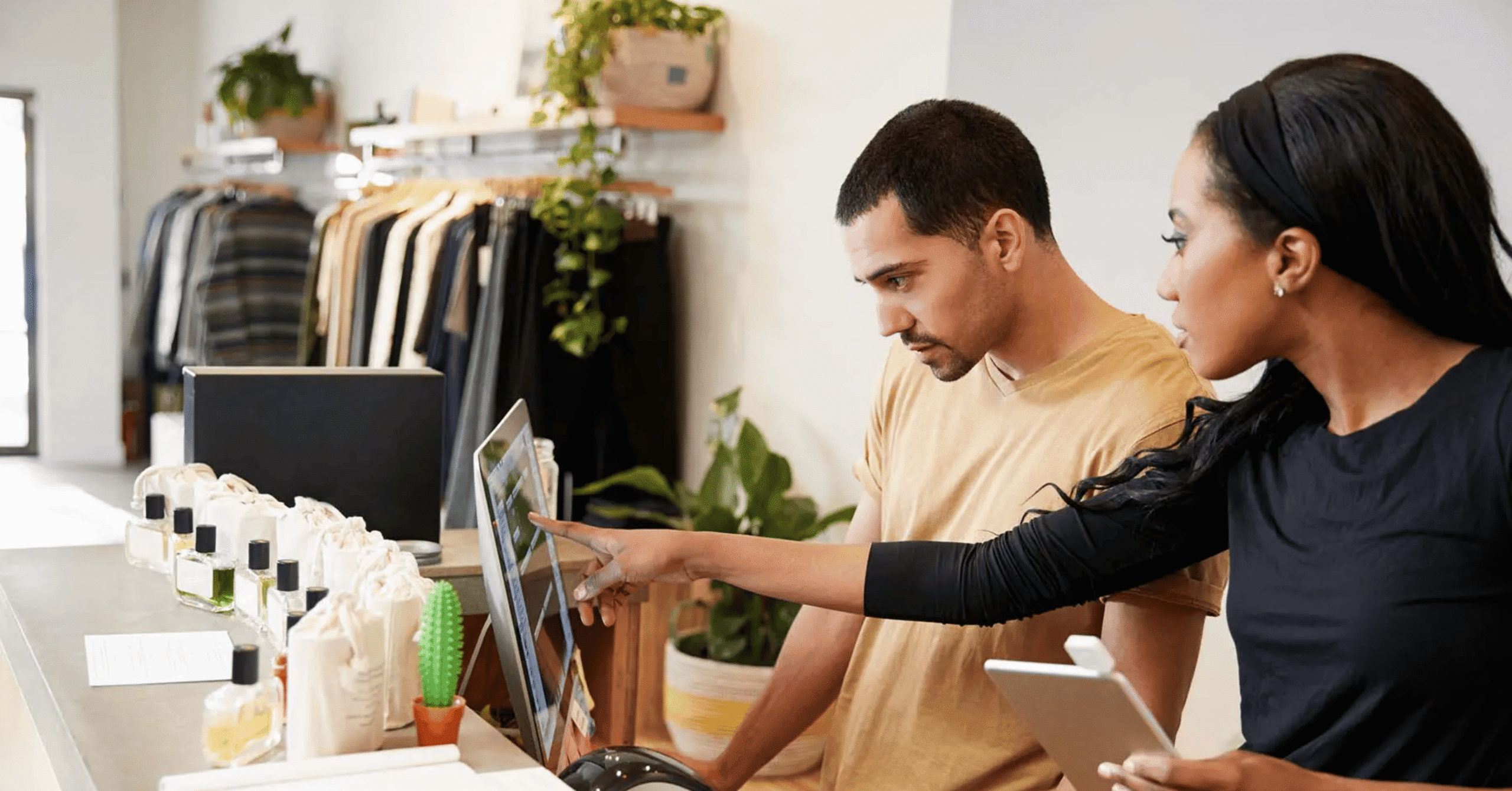 Two people stand behind a counter looking at a computer monitor, one person pointing at the screen
